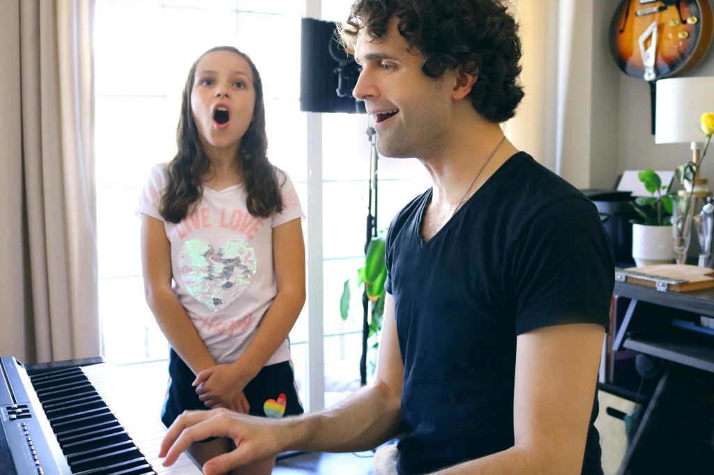 Christian Bell-Young playing the piano and singing alongside a young girl student at their home-based music studio, CBY Music.