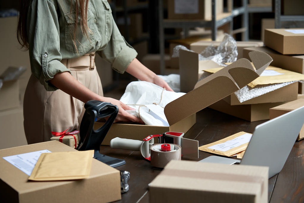 a women uses the best ecommerce platform to run her small business, packing boxes on a table