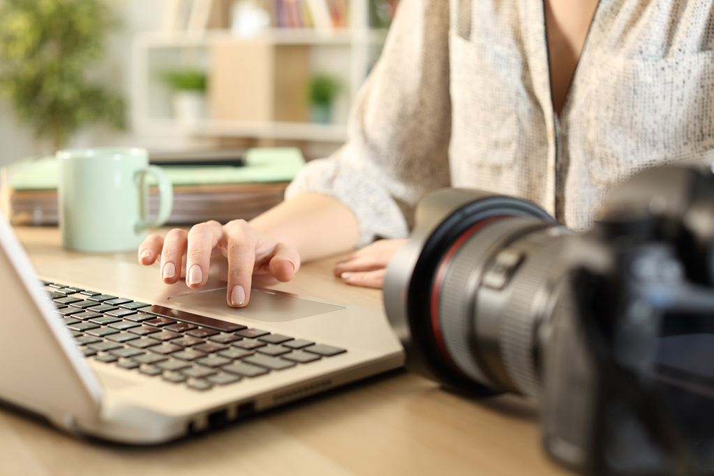 Close up of photographer woman hands connecting camera and laptop learning how to sell photos online on a desk at home