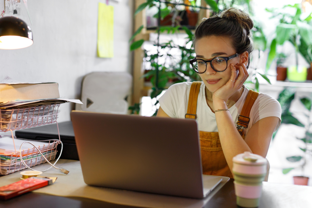 Young female gardener in glasses using laptop to make money blogging
