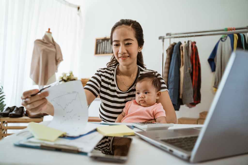 A young woman holding a kid starts a business on her laptop