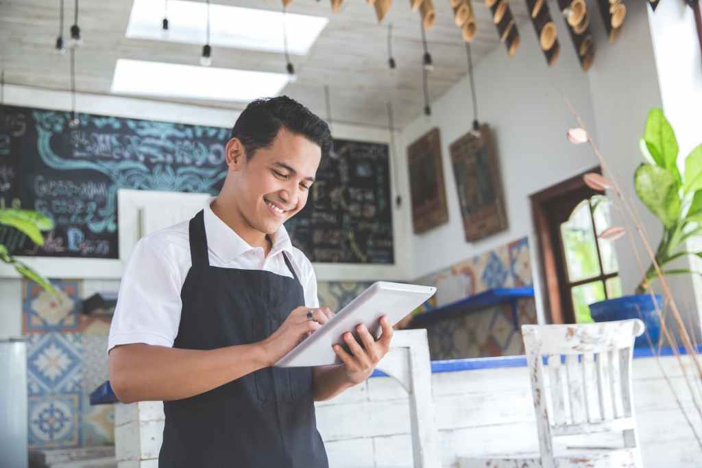 A young man in a bright cafe looks at an iPad after receiving a Canada business licence