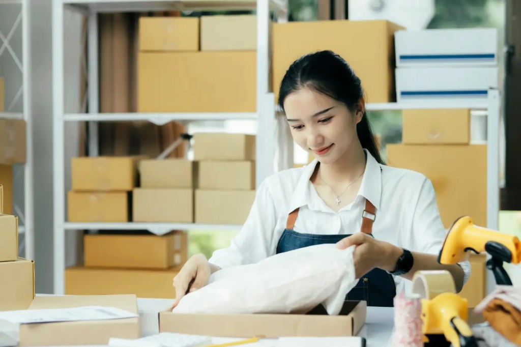 A young woman in an apron runs a business from a warehouse